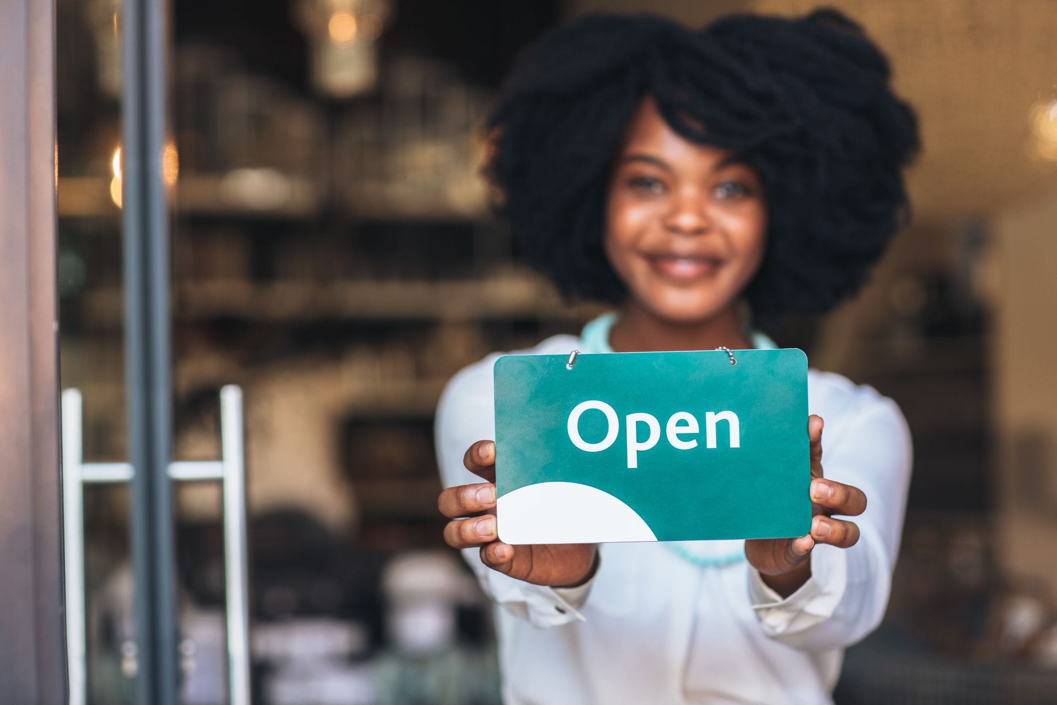 Young franchise owner proudly holding Open sign at her business