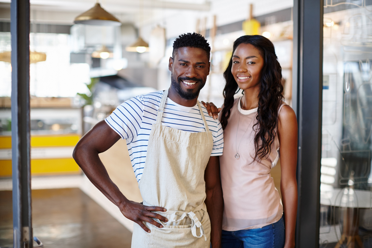 Young couple proudly standing in the doorway of their franchise business