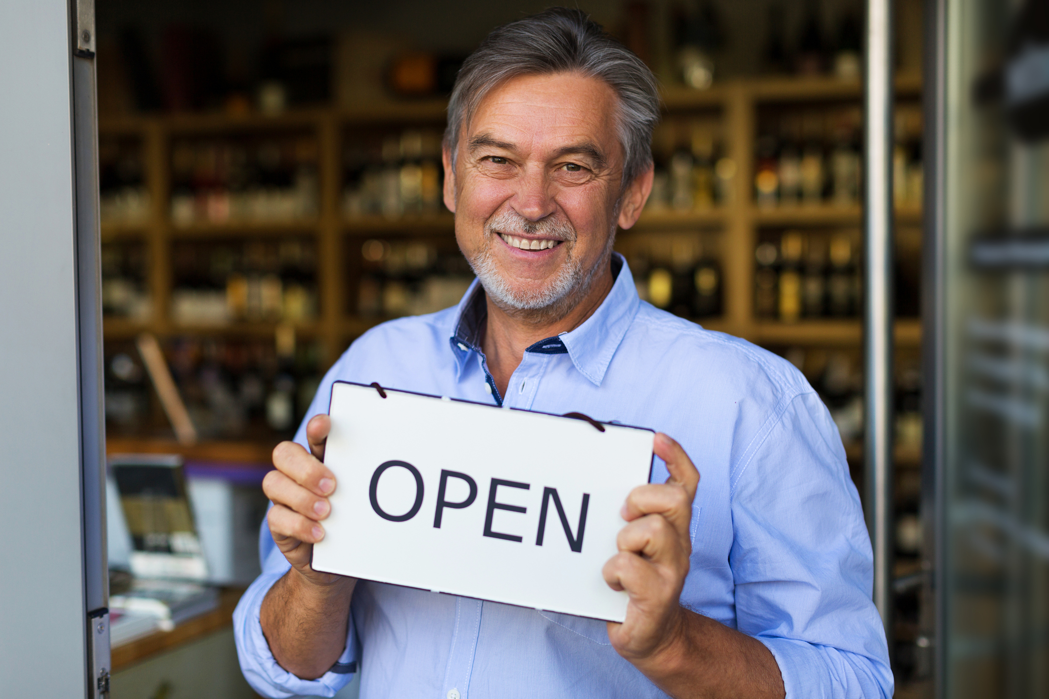 Experienced franchise owner holding Open sign at his shop