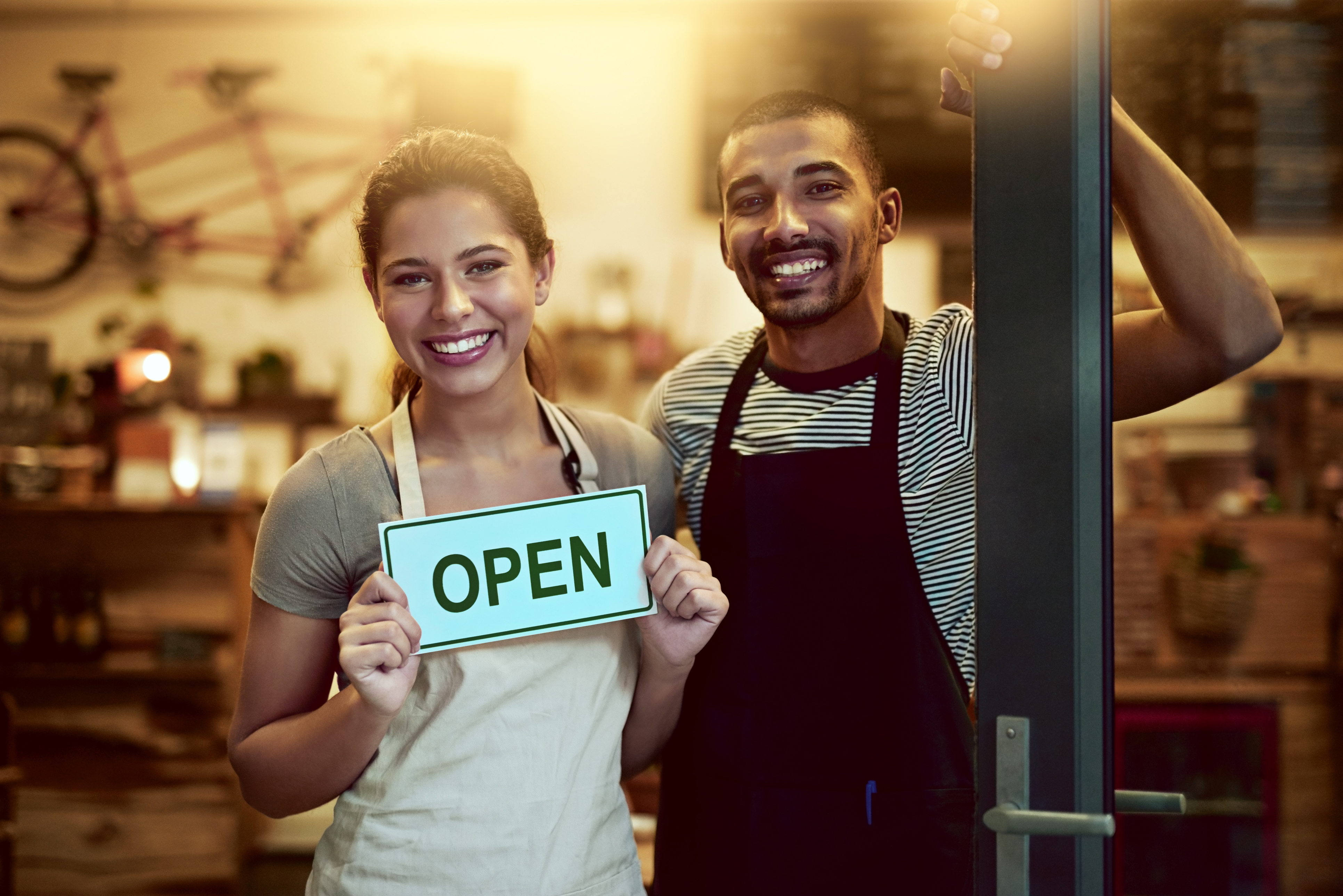 Two franchise owners proudly holding an Open sign at their business